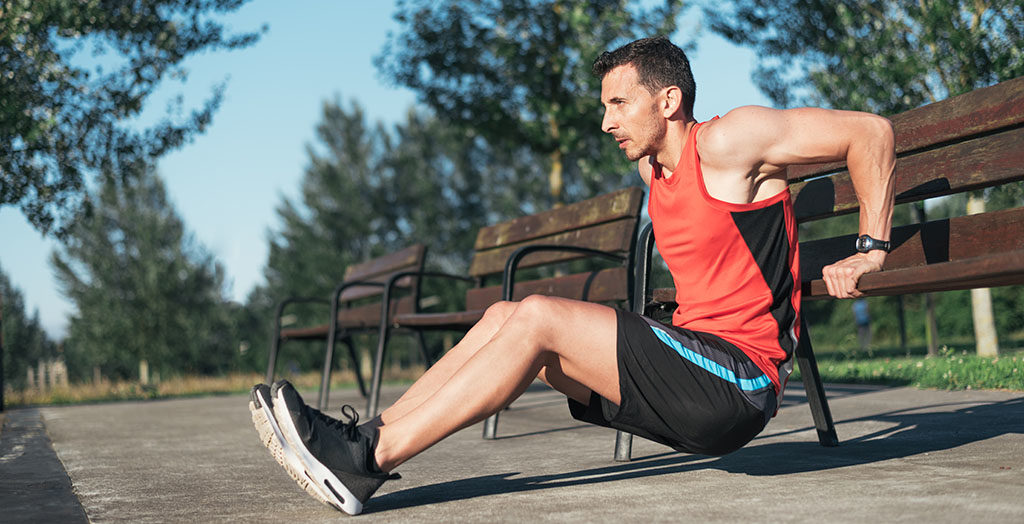 Fitness man doing bench triceps dips outdoors while working out