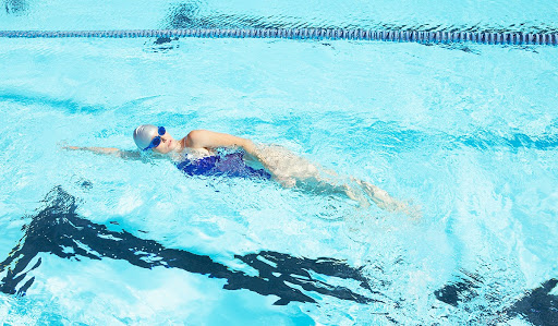 Woman in blue bathing suit, and grey swim cap swimming in a pool